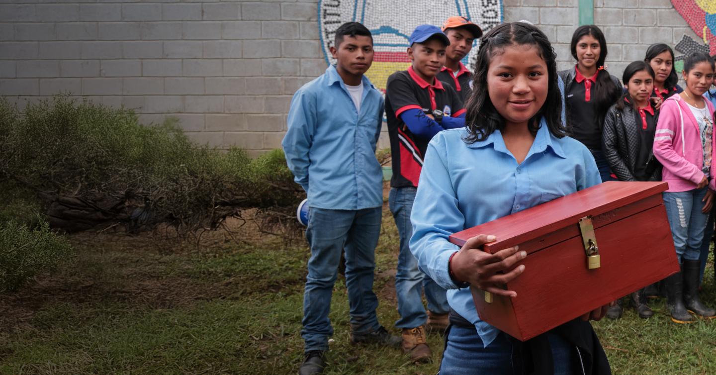 Un grupo de jóvenes. Una de ellos carga una caja de ahorros.