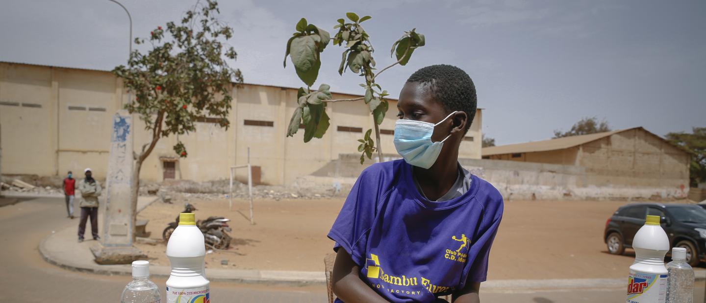 A boy wearing a medical mask sitting by a hygiene kit.