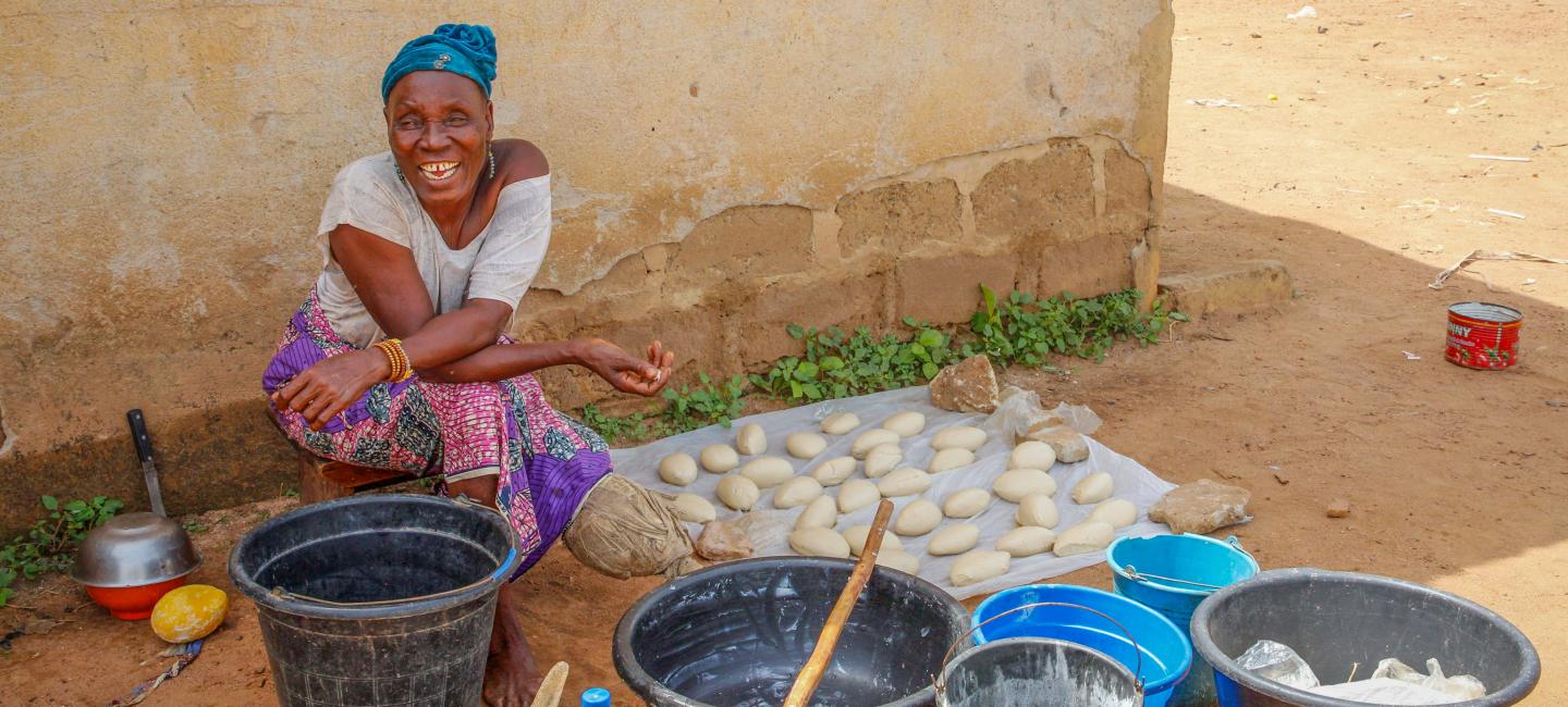 Savings group member sits outside among materials she uses to make shea butter.