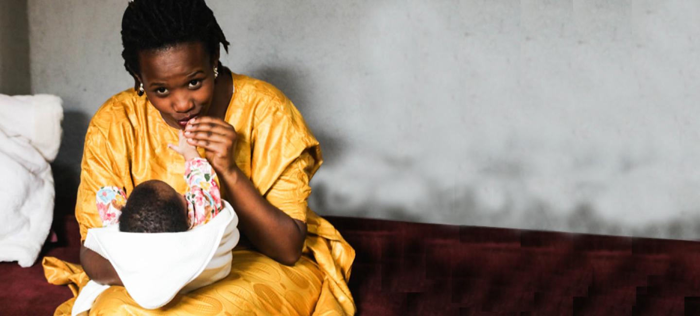 mother in yellow dress plays with infant's hands
