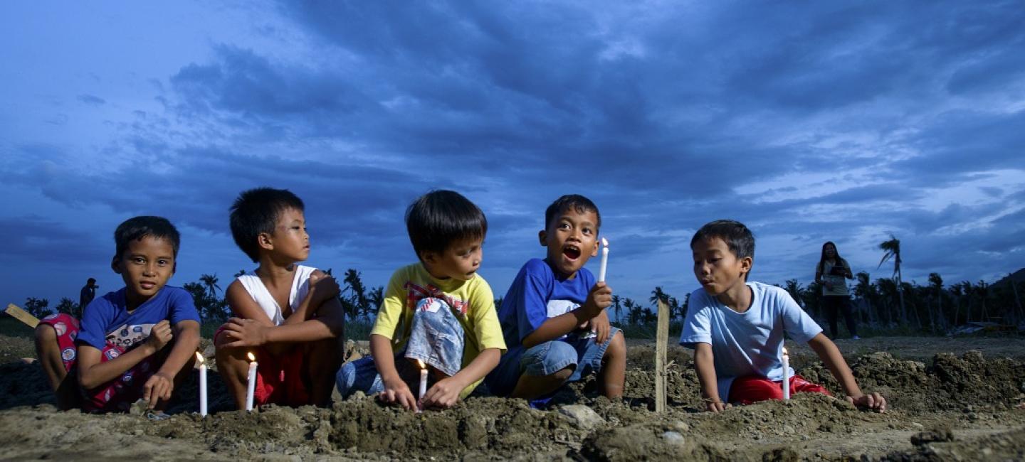 5 little boys seated outdoors in the evening with candles