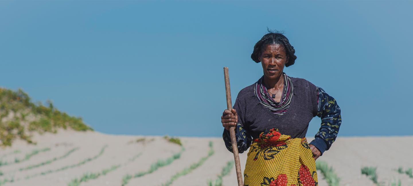 woman posing with farming tool on sand dune