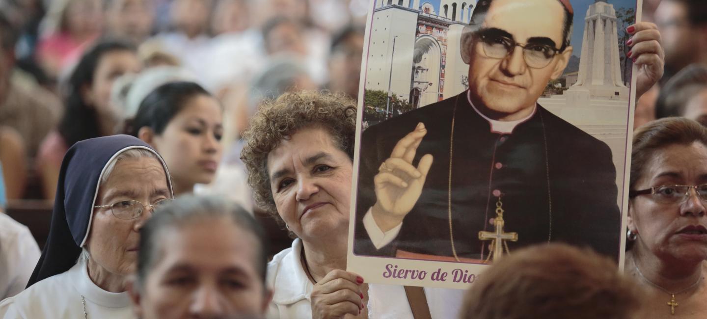 Una señora eleva una imagen de San Oscar Romero entre una multitud.