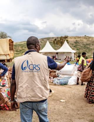 Aid worker wearing CRS vest facilitates aid at a refugee camp