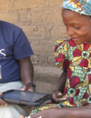 CRS staff person writing a letter with a village woman