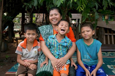 Smiling mother sits with her young son and his 2 young friends on a bench.