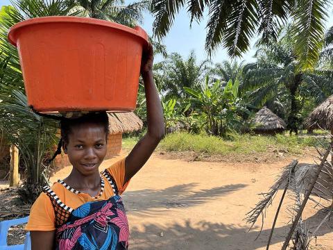A girl carrying a bin over her head.