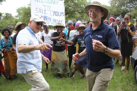 man in tan hat with blue poloshirt laughs with man in blue and white shirt