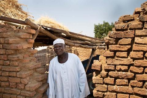 A man stands in front of a brick wall.