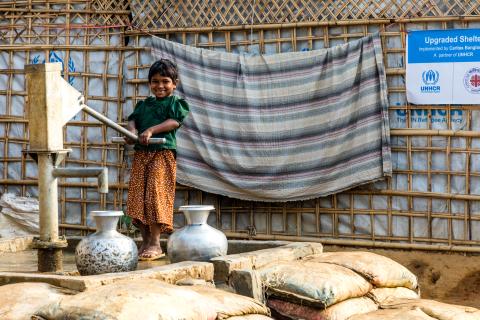 young girl in green shirt pumps water from an outdoor well
