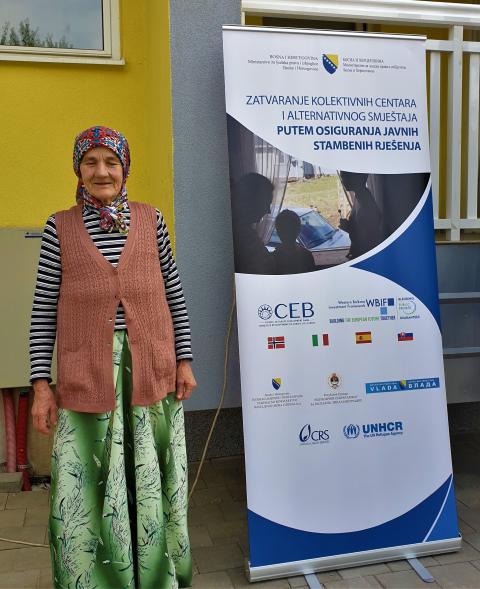 An older woman standing by a banner.