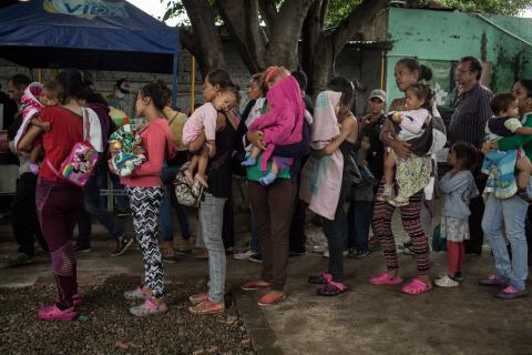 madres sosteniendo a sus hijos mientras hacen fila