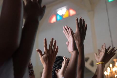 Hands held up in prayers with stained glass window in the distance