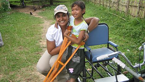 Un miembro del personal de CRS en Laos con una joven beneficiaria del proyecto en la RDP Lao. CRS le otorgó una silla de ruedas y muletas para que pueda ir a la escuela y moverse alrededor de su comunidad. Foto de personal de CRS