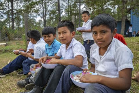 Niños en uniforme escolar comiendo sentados en el césped.