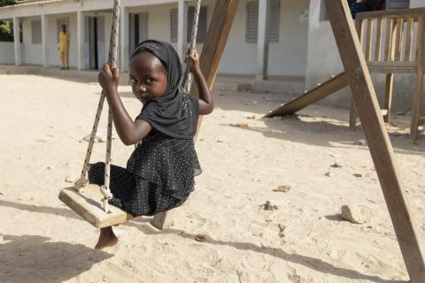 A girl wearing a black dress swinging on a playground swing.