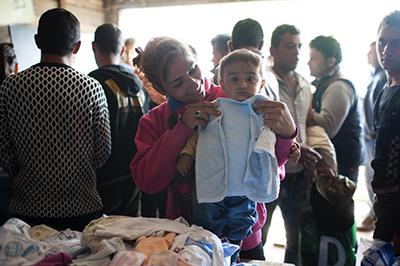 A Syrian woman looks for clothes for her baby at the Mixer House distribution center in Belgrade. Photo by Kira Horvath for CRS