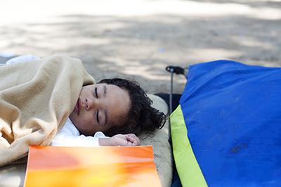 A Syrian child sleeps in a park in Belgrade, where refugees have set up a camp to rest during their long journey. Photo by Kira Horvath for CRS
