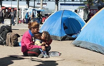 An Afghani child kisses her baby brother as her family― hoping to board buses for the Hungarian border—waits in a park next to the Belgrade bus station. Photo by Kira Horvath for CRS