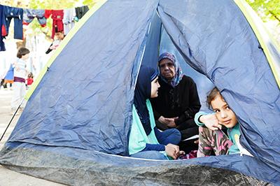 This Syrian girl waits in a tent with her mother, grandmother and sister for a bus that will take them to Hungary. The family, seeking asylum in Germany, has been traveling for more than a month. Photo by Kira Horvath for CRS