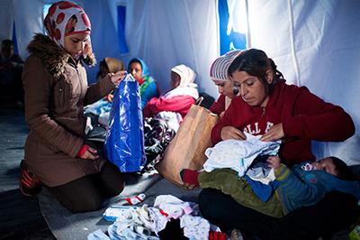 A Syrian woman looks for dry clothes for her baby. Heavy rains made the already harrowing journey to Kanjiza much more difficult. Photo by Kira Horvath for CRS