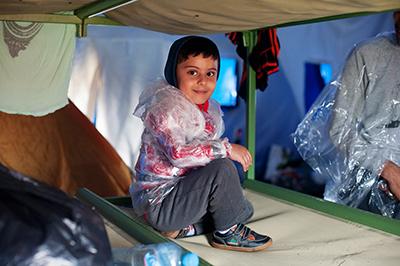 A Syrian child wears plastic bags in preparation for the wet journey to the Hungary border. Photo by Kira Horvath for CRS