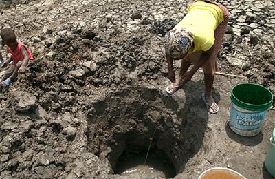 A woman and her young child  dig deep below the ground’s surface to reveal the last dregs of water. Once an abundant watering hole, the next closest source of water is hours away by foot. Photo by Nancy McNally/CRS