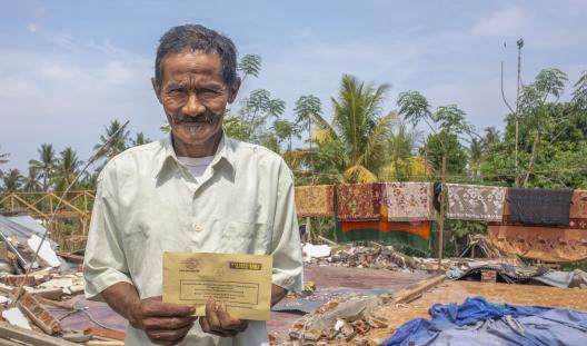 man holding cash voucher with earthquake destruction in background