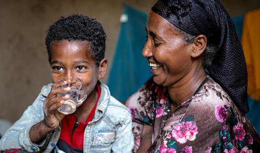 mother smiling at child drinking water from a cup