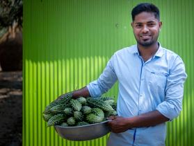 Noornobi poses in front of green wall holding a bowl of produce from his garden
