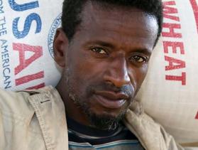 Man from Ethiopia carries a bag of food on his shoulders and looks into camera