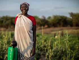 South Sudanese woman stands in field holding watering can 