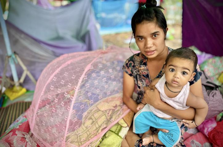 A woman holding a child while sitting on a colorful bedding under a pink mosquito net