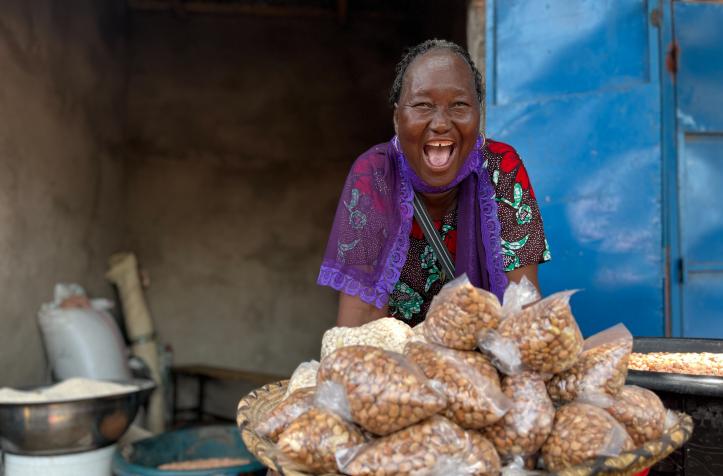 A woman wearing a colorful outfit standing behind a large basket filled with small plastic bags of nuts.