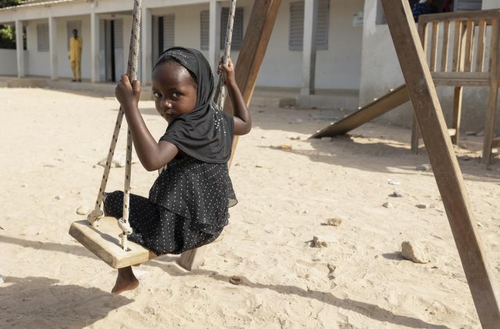 A girl wearing a black dress swinging on a playground swing.