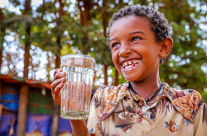 A kid holding a clear glass of water