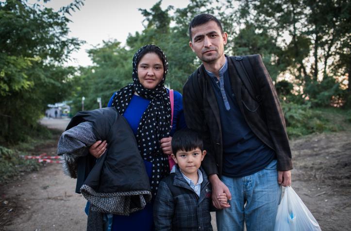 Migrant family of three standing on a dirt path. 