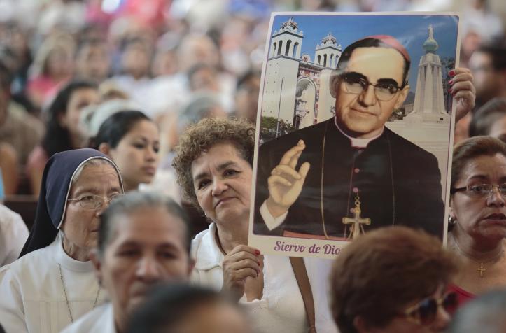 Una señora eleva una imagen de San Oscar Romero entre una multitud.