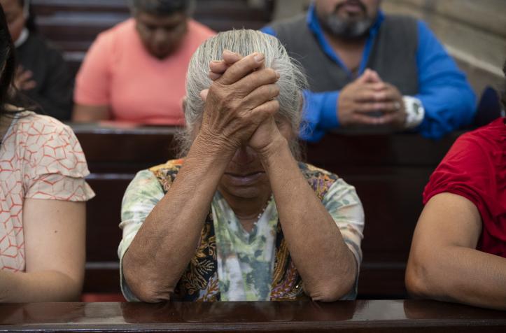 Mujer mayor orando con las manos entrelazadas en una iglesia.
