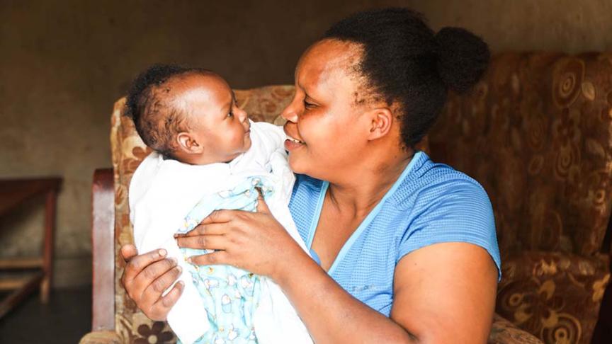 mother seated in a chair lovingly holds infant 
