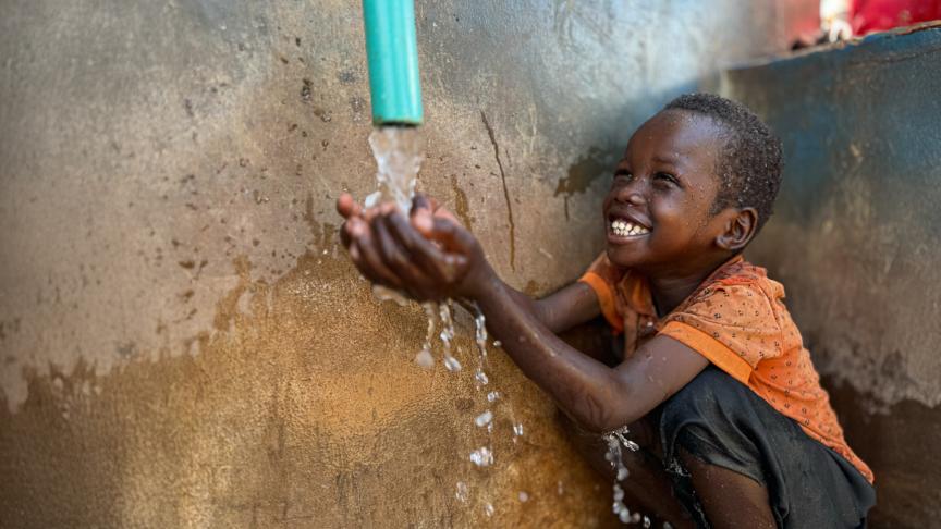 Boy smiling catching water from pump with hands