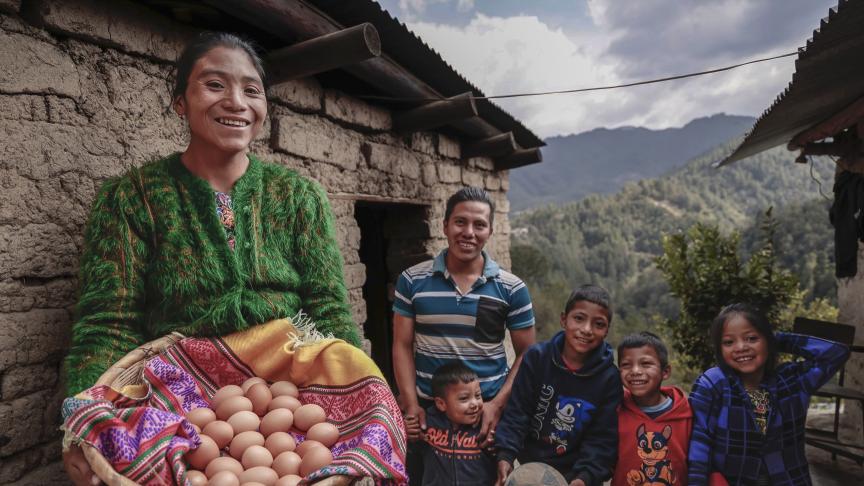 Una mujer carga una canasta de huevos. Atrás su esposo y sus hijos sonríen.